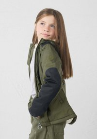 Giacca verde oliva con maniche nere, chiusura con zip e orlo elasticizzato. Caratterizzata da una fodera in pelliccia sintetica e una toppa con logo sulla spalla.