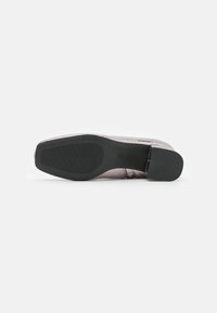 Zapato plano con parte superior metálica de oro rosa, suela de goma negra y base texturizada para agarre. Diseño simple y elegante sin hardware visible.
