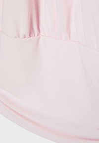 Gros plan sur un tissu rose clair avec un détail de couture froncée et une section inférieure lisse, mettant en valeur la texture et les coutures.