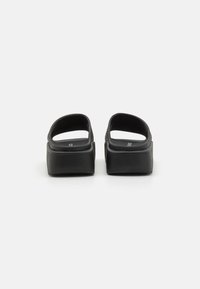 Svarte slip-on sandaler med åpen bak, mykt materiale, brede stropper og en tykk plattformsåle. Enkel design uten pynt.