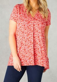 Blusa roja de flores con mangas cortas, cuello en V y un corte holgado. Presenta un pequeño patrón floral. Combinada con jeans oscuros.