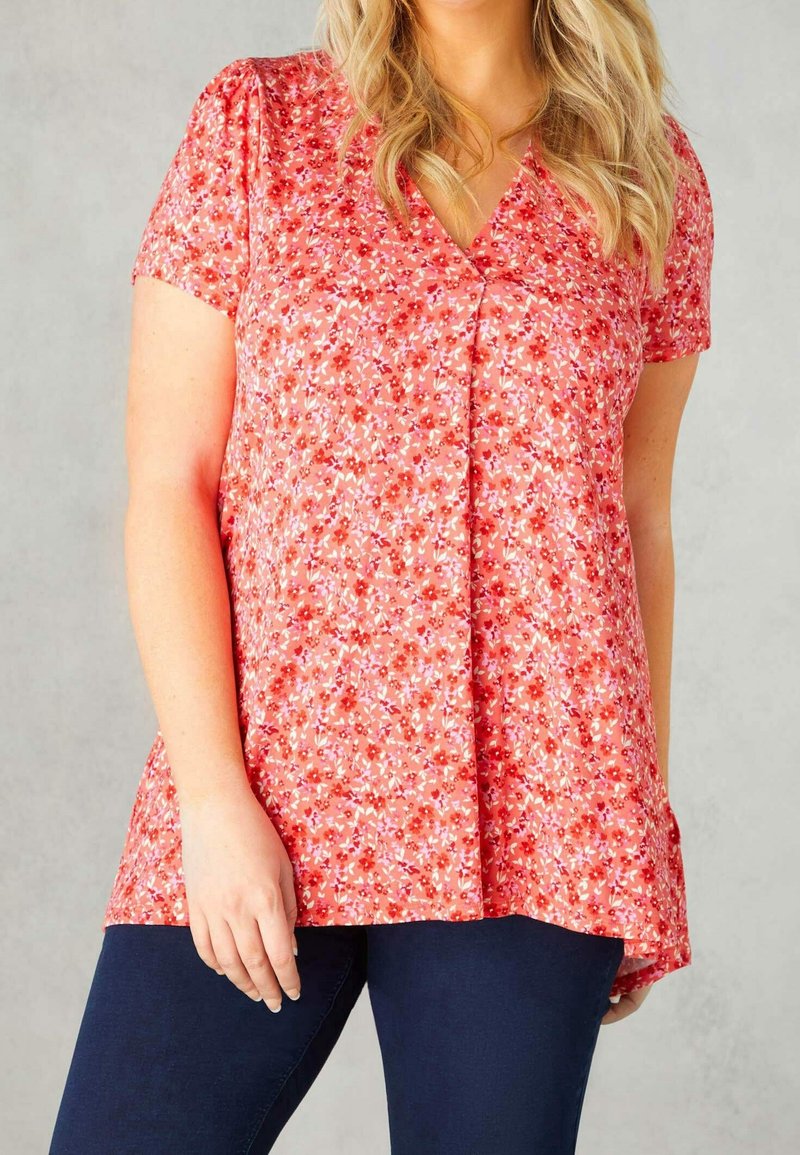 Blusa roja de flores con mangas cortas, cuello en V y un corte holgado. Presenta un pequeño patrón floral. Combinada con jeans oscuros.