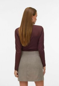 Vinrød langermet topp kombinert med et lyst grått, skreddersydd skjørt. Toppens tekstur er jevn, mens skjørtet har et subtilt vevmønster.