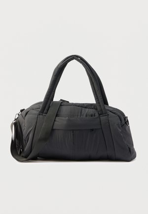 Black padded duffel bag with dual handles and an adjustable shoulder strap on a plain light background.