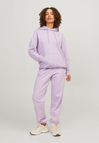 Lilla hettejakke med snor og kengurulomme, sammen med matchende joggebukser. Myk stoff med ribbede mansjetter, brukt med lette sneakers.