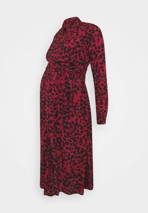 Robe de maternité à manches longues bordeaux avec des taches noires abstraites, col à revers et ceinture à nouer à la taille.