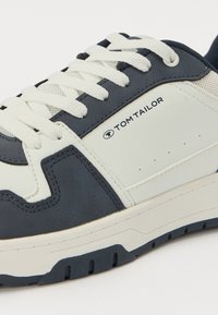 Zapatillas con un diseño en azul marino y blanco, materiales de cuero y malla, cordones planos blancos, perforaciones y un logo de marca en el lateral.