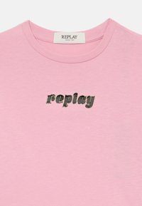 Lyserød bomulls t-skjorte med rund hals og korte ermer. Har en sølvfarget metallisk "replay"-logo på forsiden.