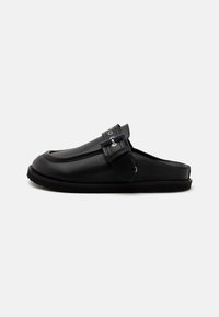 Chaussures noires à enfiler en cuir lisse, avec une sangle avant ornée d'une boucle métallique et une semelle texturée pour une meilleure adhérence.