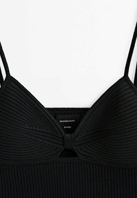 Haut en tricot noir avec une texture côtelée, de fines bretelles réglables et un détail en nœud à l'arrière. Étiquette indiquant "Massimo Dutti Studio."