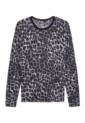 Person iført en langærmet leopardprint-top, lysegrå højttaljede jeans med rå kanter og sorte spidse hæle, armene krydset.