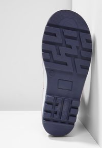 Sko yttersula i mörkblå gummi, med ett texturerat zigzag-mönster, en cirkulär logotyp och en rektangulär indragning för stabilitet.