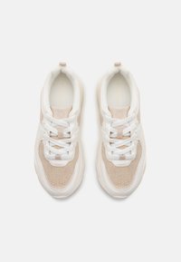White sneakers with beige mesh panels, featuring round toe, thick white soles, white laces, and a glossy beige accent at heel.