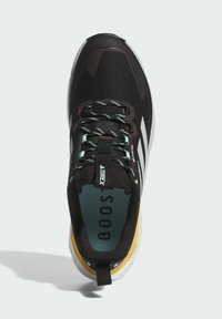 Chaussure de sport noire avec une tige en maille, des accents blancs et une semelle rembourrée. Présente des détails texturés et des lacets colorés.
