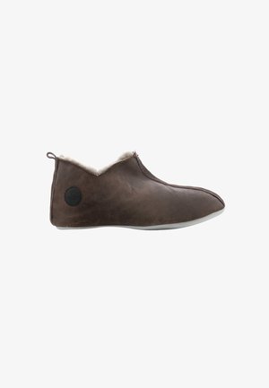 Bruine zachte leren pantoffel met witte fleece voering, zijrits, platte zool en een kleine ronde zwarte logopatch op de hiel.
