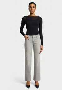 Body de manga longa preto com decote quadrado, combinado com jeans retos cinza claro e saltos agudos pretos, de pé contra um fundo neutro.