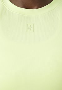 Lichtgroene sporttop met geribbelde textuur, met een ronde halslijn en een klein reliëflogo op de borst.