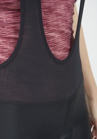 Zwarte sporttanktop met een gestructureerde mesh halslijn en een aansluitend, glad zwart lijfje, gecombineerd met een bordeauxrode, gestreepte onderlaag die zichtbaar is eronder.