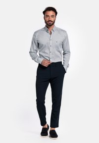 Overhemd met knoopsluiting en geometrisch patroon in wit en marineblauw, gecombineerd met donkerblauwe broeken. Heeft een slim fit en casual zwarte schoenen.
