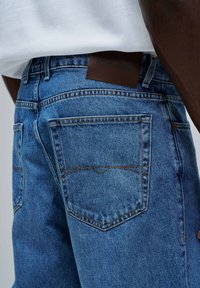 Jeans de mezclilla en azul medio con un parche de cuero en la parte trasera etiquetado "Salsa Jeans" y costuras de contraste en los bolsillos. Corte estándar con dos bolsillos traseros.
