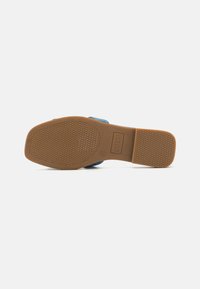 Blue sandal with a textured, brown rubber sole. Features a flat heel and a smooth upper design. Logo details on the sole.