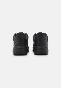 Svarta sportskor med slätt läderöverdela, vadderad krage och texturerad gummisula. Har en bakre flik för enkelt av och på.