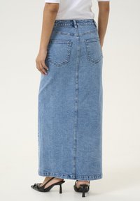 Denim maxi skirt in light blue, featuring back pockets, a straight cut, and a hemline that reaches the ankles. Paired with black heeled sandals.