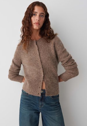 Bruine gebreide cardigan gemaakt van zachte stof, met een ronde halslijn, lange mouwen en knoopsluiting aan de voorkant. Draagt met blauwe jeans.