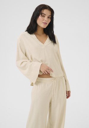 Beige loungewear set featuring a V-neck top with bell sleeves and loose-fitting drawstring pants. Soft, textured fabric with a relaxed fit.