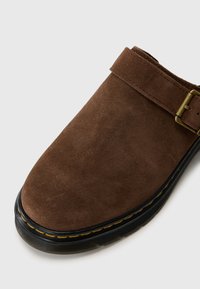 Scarpa slip-on in suede marrone con punta rotonda, caratterizzata da una fascia decorativa e suola in gomma nera con cuciture gialle.