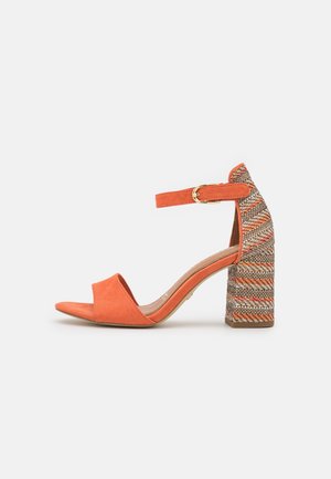 Sandalia de ante naranja, abierta en la punta, con correa en el tobillo y tacón ancho tejido multicolor decorativo sobre fondo blanco.