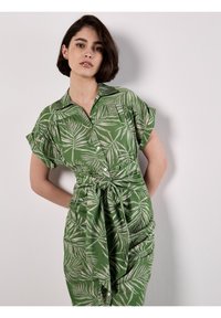 Grünes Hemdkleid mit kurzen Ärmeln, das ein Palmblattmuster aufweist und einen gebundenen Bund hat. Hergestellt aus leichtem Stoff mit einer strukturierten Oberfläche.