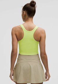 Neon-gelbes geripptes Cropped-Top mit breiten Trägern und einem taillierten Design, kombiniert mit einem hellbeigen ausgestellten Rock. Glatte Textur, minimalistische Details.