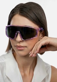 Paarse oversized zonnebril met een transparant montuur en donkere lenzen, met een geometrisch ontwerp en hoekige vorm.