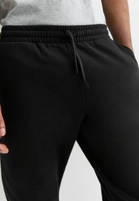 Zwarte trainingbroek met een zachte textuur, elastische tailleband en verstelbare trekkoord. Voorzien van zijzakken en een gestroomlijnde pasvorm.