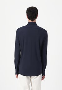 Marineblaues Langarmhemd mit geradem Schnitt, knöpfbaren Manschetten und subtiler glänzender Optik. Glattes Material; die Rückansicht zeigt den Kragen und ein nahtloses Design.