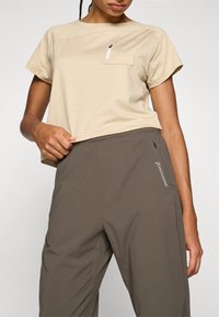 Beige T-shirt met korte mouwen met een gestructureerde afwerking en zijzak; gecombineerd met grijze, lichte broek met elastische taille met een zijlogo.