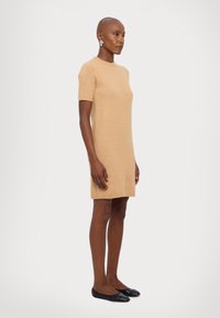 Short-sleeve, knee-length dress in light tan knit fabric, featuring a round neck and a relaxed fit, paired with black ballet flats.