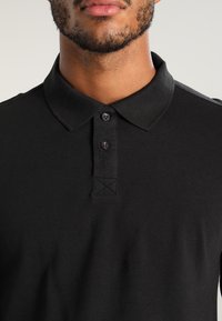 Zwarte poloshirt van gestructureerde katoen, met een klassieke kraag, een drie-knopen sluiting en stiksels details bij de halslijn.