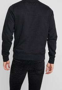 Sudadera negra con cuello redondo, mangas largas y puños y dobladillo acanalados. Textura suave sin logos ni estampados visibles.