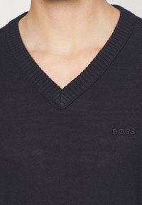 Dunkelblaues V-Neck-Pullover, aus gestricktem Material, mit geripptem Kragen, versehen mit dezentem "BOSS"-Logo, das auf der linken Seite gestickt ist. Weiche Textur.