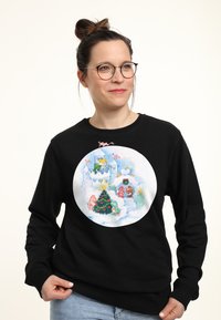 Il sudore nero presenta una grafica circolare colorata con una scena invernale, inclusa una albero di Natale e personaggi giocosi su uno sfondo nevoso.