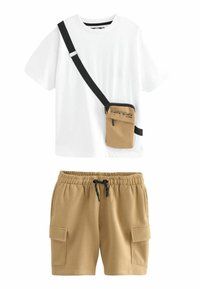 Camisa blanca de cuello redondo, combinada con pantalones cortos de carga color beige que tienen bolsillos laterales y una cinturilla elástica, además de un pequeño bolso cruzado color beige.
