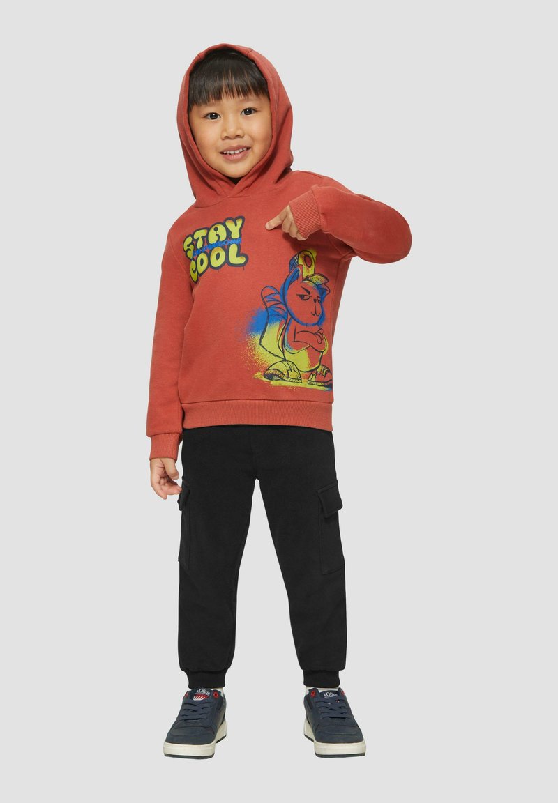Rode hoodie met de tekst "STAY COOL" en een cartoonfiguurontwerp; gecombineerd met zwarte cargobroek en donkere sneakers.