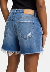 Lichte blauwe denim shorts met een rafelige zoom, verwerkte details en een patch op de achterste tailleband. Voorzien van standaard achterzakken.