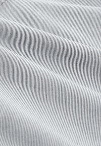 Gros plan d'un tissu blanc avec de fines rayures noires verticales et des plis doux créant des ombres délicates.