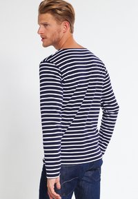 Marineblå og hvide stribede langærmede skjorte med rund halsudskæring. Glat stof, tæt design og synlige syninger på ryggen.