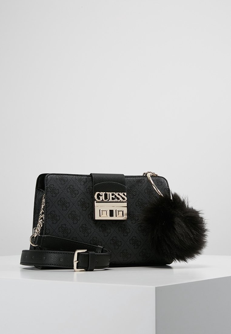 Sort Guess handbag med tekstureret materiale, guldhardware, logo-plade og aftagelig pels pom-pom. Inkluderer en aftagelig rem.