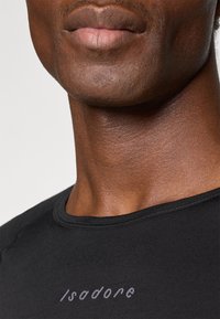 Czarna sportowa koszulka z okrągłym dekoltem i krótkimi rękawami, z delikatnym szarym logo "Isadore" nad kołnierzem. Gładka faktura.