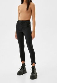 Jeans negros ajustados con cintura alta, con detalles de dobladillo deshilachado. Combinados con una camiseta de manga larga de canalé beige y botas negras gruesas.